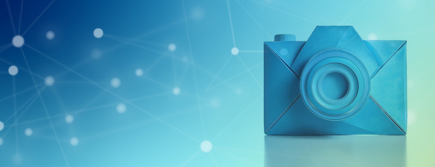 Eine blaue Origami-Kamera liegt auf einer glänzenden Oberfläche vor einem Hintergrund mit Farbverlauf, und abstrakten verbundenen weißen Punkten, die einem digitalen Netzwerk ähneln.
