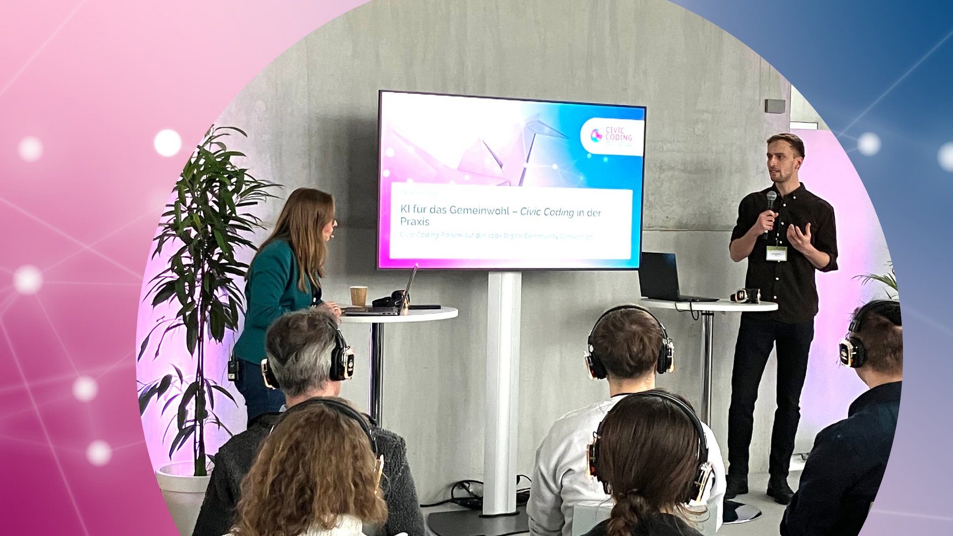 Rafael Bendzus (BMUV) und Ina Gamp (Geschäftsstelle Civic Coding) stehen vor einem Raum mit einem Präsentationsbildschirm, auf dem KI für das Gemeinwohl – Civic Coding in der Praxis zu sehen ist. Mehrere sitzende Teilnehmer tragen Kopfhörer.