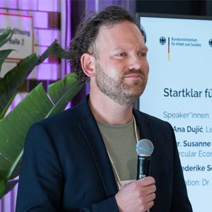 Dr. Julian Stubbe mit einem Bildschirm in Hintergrund
